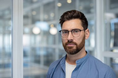 Kendine güvenen ciddi bir iş adamının portresi. Bir adam düşünceli bir şekilde kameraya bakar. Şirket müteahhitlerinden biri ofisteki işyerine yakın çekim yapmış..