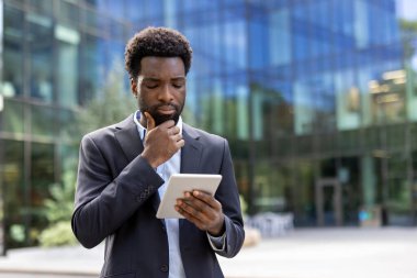 Ofis binasının dışında elinde tablet bilgisayarla ciddi düşünen bir iş adamı. Afrikalı Amerikalı adam, finansör yatırımcı şehirde dolaşıyor, internette kitap okuyor..