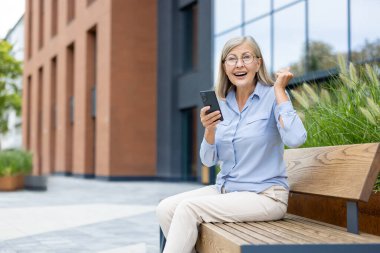 Keyifli bir son sınıf öğrencisi, akıllı telefonuyla bankta otururken seviniyor ve bu habere şaşırıyor..