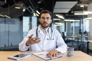 Webcam görüntüsü, doktor hastalara uzaktan danışmanlık yapıyor. Beyaz önlüklü adam, online konferans toplantısı için görüntülü görüşme yapıyor. Ciddi doktor tedavinin gidişatını açıklıyor.