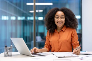 İşyerindeki başarılı kadın finansörün portresi. İş kadını gülümseyen ve kameraya bakan belgeleri imzalıyor. Muhasebeci raporları hazırlar ve vergi formlarını doldurur..