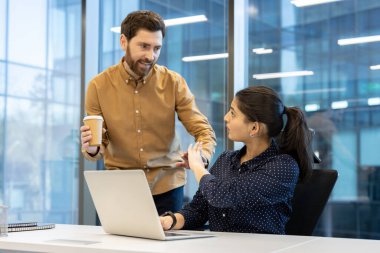 Bir kadın, elinde kahve fincanı olan bir adamı durdurmak için elini kaldırıyor ve potansiyel olarak işyeri tacizini resmediyor.
