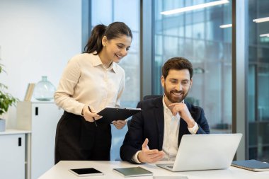 İki meslektaş bir proje üzerinde işbirliği yapıyorlar, parlak, modern ofis ortamında bir dizüstü bilgisayardaki bilgileri gözden geçiriyorlar..