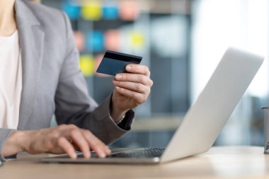 İnternetten alışveriş yapan bir kadın, ofisteki kredi kartını ve laptopunu kullanarak masasının rahatlığından güvenli alışverişler yapıyor.