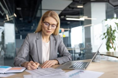 Ofis içinde evrak işleriyle uğraşan ciddi odaklı bir kadın. İş kadını finansör muhasebeci mali rapor hazırlıyor ve vergi formlarını dolduruyor. Belgeleri düşünen bir ofis çalışanı..