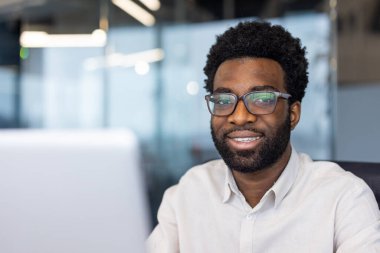 Ofis ortamındaki dostane ve kendinden emin tavrını gösteren gülümseyen bir profesyonelin yakından çekimi..