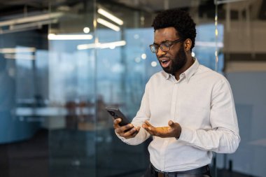 Gözlüklü bir Afrikalı Amerikalı ofis ortamında telefonunda gördüğü bir şeye şaşırır..