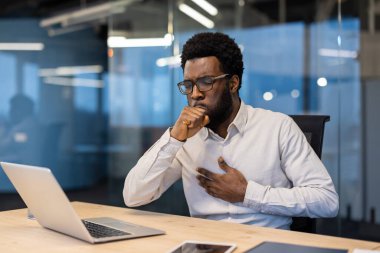 Modern ofisteki endişeli bir Afro-Amerikalı hasta ve bilgisayarında çalışırken öksürüyor..