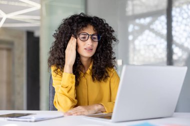 Genç bir iş kadını dizüstü bilgisayarında çalışırken stres yaşıyor. Gerilim ve rahatsızlık belirtileri gösteriyor.