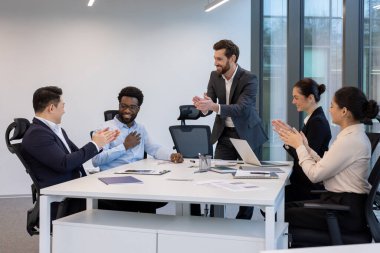 Konferans masasındaki çeşitli bir grup meslektaşı ofis başarısını takım çalışması ve işbirliği ile kutlayan bir iş arkadaşını alkışladı..