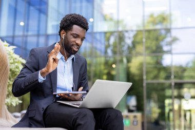 Kendinden emin bir Afro-Amerikalı işadamı bilgisayarında sanal bir toplantıya katılıyor, meslektaşlarını selamlıyor ve bir deftere notlar yazıyor..