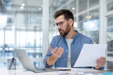 Gözlük takan bir işadamı, ofis ortamında çalışırken kafası karışmış ya da hayal kırıklığına uğramış görünüyor..