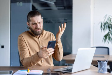 Hüsrana uğramış bir adam akıllı bir telefon tutar, masasında otururken kafası karışmış ya da çileden çıkmış gibi görünür. Bir dizüstü bilgisayar ve ofis malzemeleri görünür..