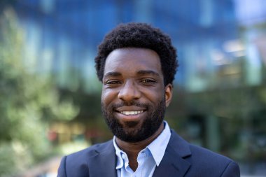 Takım elbiseli gülümseyen bir zencinin portresi. Yeşil arka planda ve dışarıda çekilmiş bir bina..