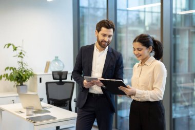 Modern ofis ortamında çeşitli profesyonellerden oluşan bir ekip, belgeleri gözden geçirir ve birlikte tablet kullanır, odaklanmış bir çalışma ortamı yaratır..