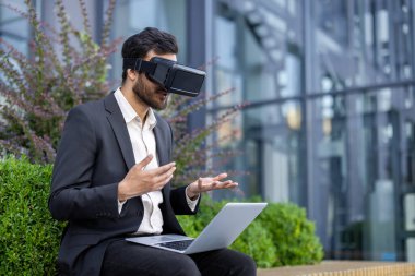 Bilgisayarlı VR gözlük takan bir işadamı dışarıda otururken işaret ediyor, modern teknoloji konsepti..
