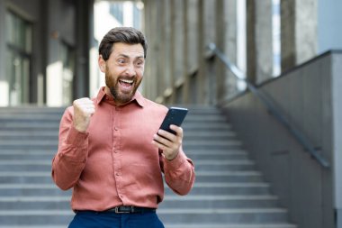 Telefonunu tutup tezahürat yapan heyecanlı bir adam bir binanın önünde duruyor. Adam telefonunda gördüğü bir şeyden dolayı mutlu görünüyor..