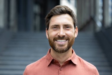 Sıcak bir gülümsemesi olan neşeli bir adam binanın önünde taş bir merdivenle pozitiflik saçıyor..