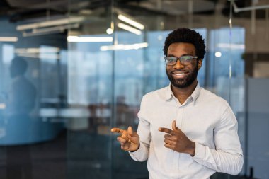 Dost canlısı, gülümseyen gözlüklü bir adam modern ofis ortamında pozitifliğini gösteriyor..