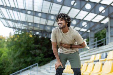 Mide ağrısından muzdarip bir sporcu aktif fiziksel egzersiz ve koşu sırasında karnının kenarını tutuyor..