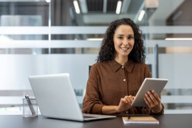 Ofisin içinde ofisin içinde başarılı, neşeli bir iş kadınının portresi. Başarılarının sonuçlarından memnun olan şirket çalışanı, bir tablet bilgisayarda bir uygulama kullanıyor..