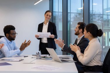 Bir iş kadını toplantıda hazır bulunurken, meslektaşları da takıma olan katkılarından ötürü alkışlıyorlar. Başarıyı kutluyorlar..