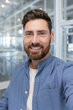 Mavi gömlekli, gülümseyen, sakallı bir adam, dostça ve cana yakın tavrını sergiliyor..