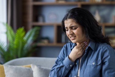 Evdeki kanepede oturan, elini boynuna dayamış, boğazı ağrıyan hasta genç bir kadının yakın plan fotoğrafı..