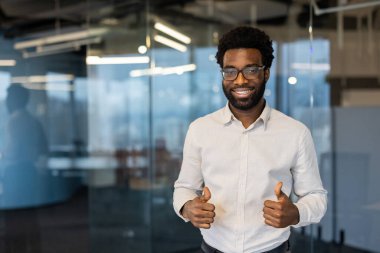 Gözlüklü, gülümseyen Afrikalı Amerikalı bir adam ofis ortamında başarı ve onayı temsil ediyor..