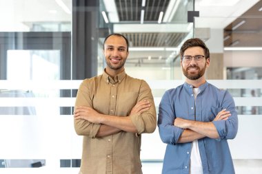 İki kendine güvenen adam, kollarını kavuşturup kameraya gülümsüyor. Profesyonel bir tavır sergiliyorlar..