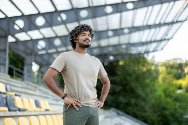 Bir atlet elleri kalçasında, gözleri kapalı durur. Fitness egzersizinden sonra ara vermiş gibi görünüyor..