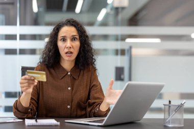 Şaşırmış bir kadın dizüstü bilgisayarın önündeki kredi kartına bakar. Çalışırken hayal kırıklığına uğramış ya da kafası karışmış görünüyor..