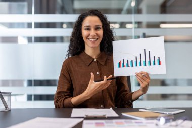 Gülümseyen bir kadın, bir ofis ortamındaki sunum sırasında grafiğe işaret eder. İş, veri analizi.
