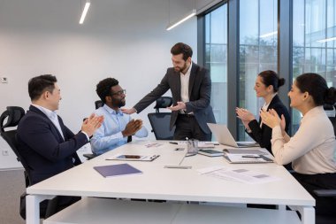 Çeşitli bir ekip, modern bir ofiste başarıyı alkışlar ve liderleri ile kutluyor..