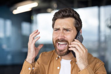 Stresli bir adam telefonuna bağırıyor, yakın çekimde hayal kırıklığı ve öfke gösteriyor..