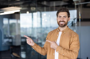 Zeki kıyafetli gülümseyen bir adam iki eliyle bir yeri gösterir, muhtemelen bir şey gösterir..