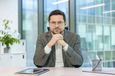 Takım elbiseli ve gözlüklü genç, başarılı ve ciddi bir adamın portresi ofisteki bir masada oturmuş, kendine güvenle kameraya bakıyor..