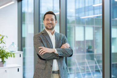 Spor ceketli kendine güvenen bir işadamı, kollarını kavuşturmuş, profesyonellik ve başarı saçarak poz veriyor..