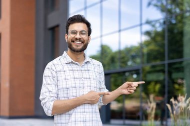 Sokakta tişörtlü genç bir Hintli 'nin portresi. Parmaklarıyla boş bir yeri işaret ediyor. Kameraya gülümsüyor..