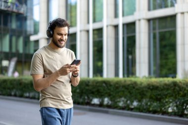 Genç bir adam kulaklıkla müzik dinlerken koşmaktan, akıllı telefonuna bakmaktan ve gülümsemekten zevk alır..