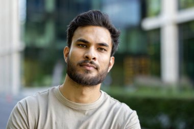 Sakallı ve tarafsız bir yüz ifadesi olan genç bir adamın portresi, muhtemelen egzersiz yaptıktan sonra. Şehir arkaplanı.