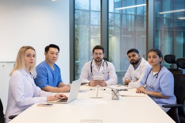 Modern bir ofiste, masada oturan çeşitli tıp uzmanları bir araya gelip....