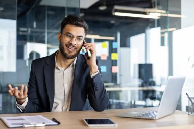 Genç bir işadamı modern bir ofiste çalışırken telefonla konuşur..
