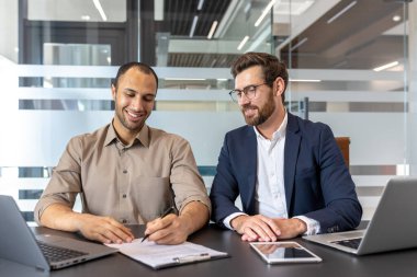 İki işadamı bir masada oturuyor, biri bir belge imzalarken diğeri izliyor. Mutlu görünüyorlar..