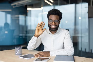 Ofisteki bir masada otururken gözlüklü ve gülümseyen Afro-Amerikalı bir adam. Mutlu ve cana yakın görünüyor..
