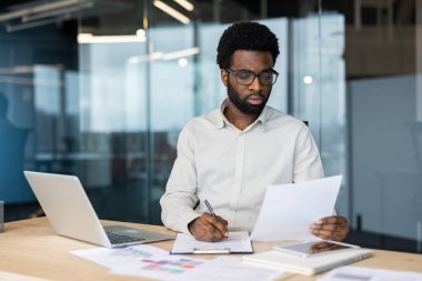 Afrika kökenli Amerikalı bir işadamı, evrak işlerine odaklanmış ve gün içinde bilgisayarının başında çalışıyor..