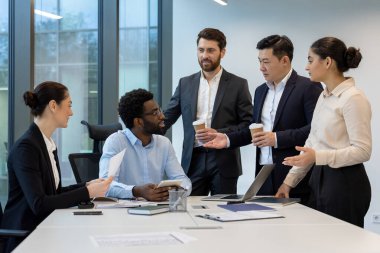 Modern ofis ortamında, bir dizüstü bilgisayar ve bir masanın üzerindeki belgelerle meşgul olan çeşitli iş adamları..
