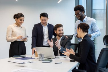 Çeşitli iş adamları modern ofis ortamında bir başarıyı kutluyor. Meslektaşlar masanın etrafında toplanır, alkışlar ve işbirliği yaparlar..