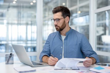 Profesyonel bir adam, masa başında oturuyor, evrak işleri, dizüstü bilgisayar ve ofiste çalışıyor..
