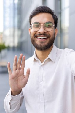 Binanın dışındaki video görüşmesinde sakallı ve gözlüklü bir adam el sallıyor.